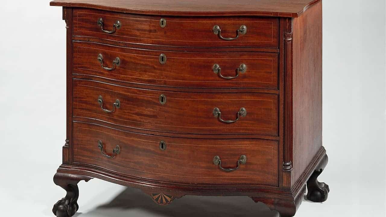 Federal style mahogany chest of drawers with four drawers, brass handles, decorative columns, and curved legs on white background