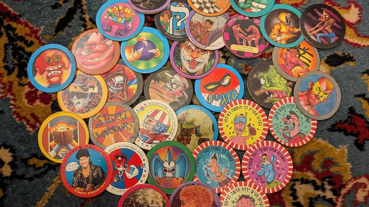 Collection of vintage Pogs game discs with colorful cartoon characters, monsters, and pop culture imagery scattered on patterned rug