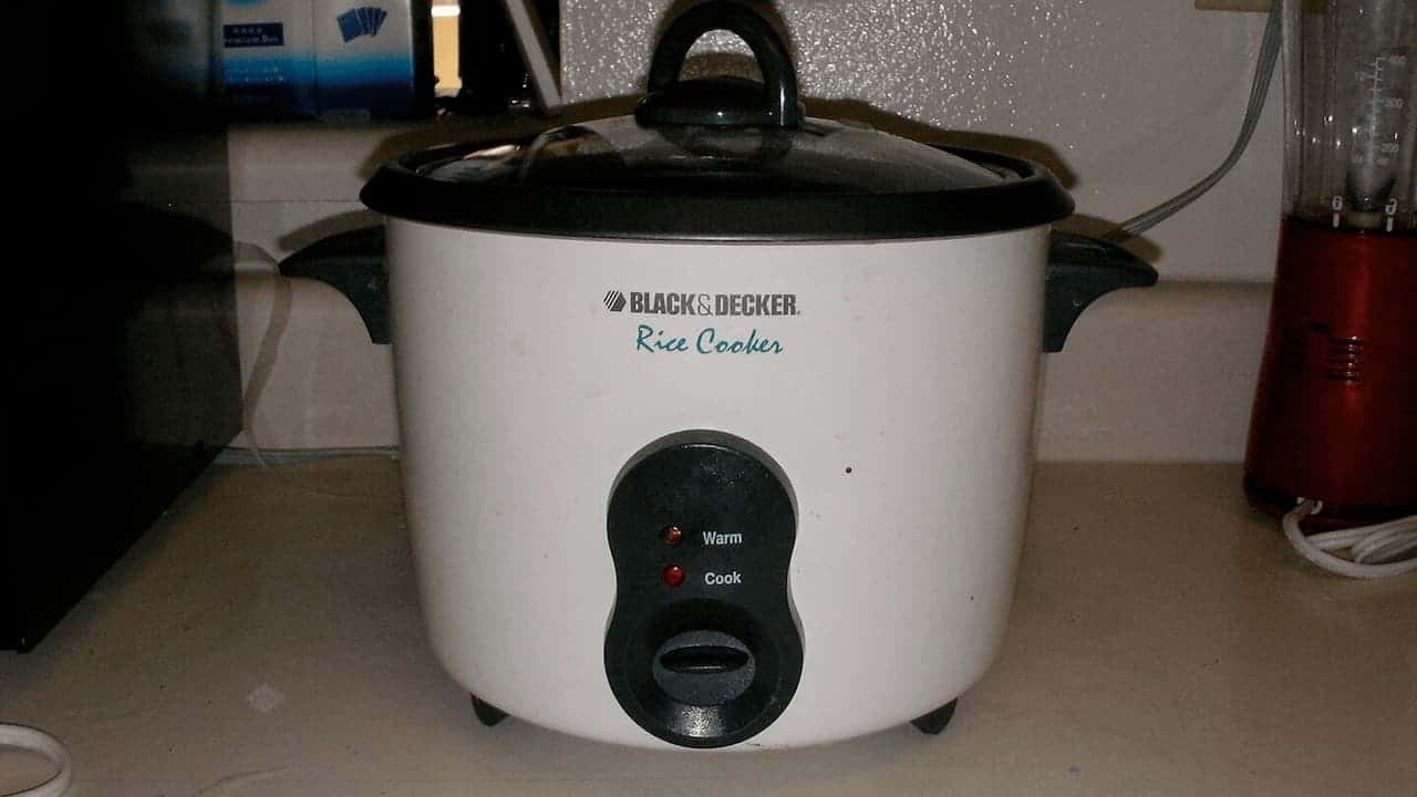 White Black & Decker rice cooker with black lid and control panel showing "Warm" and "Cook" settings on kitchen counter