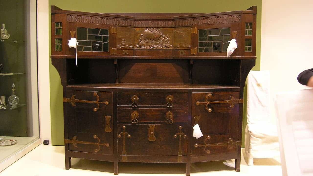 Dark wood Victorian sideboard with ornate carved details, multiple doors and drawers, decorative brass hardware, displayed in museum setting