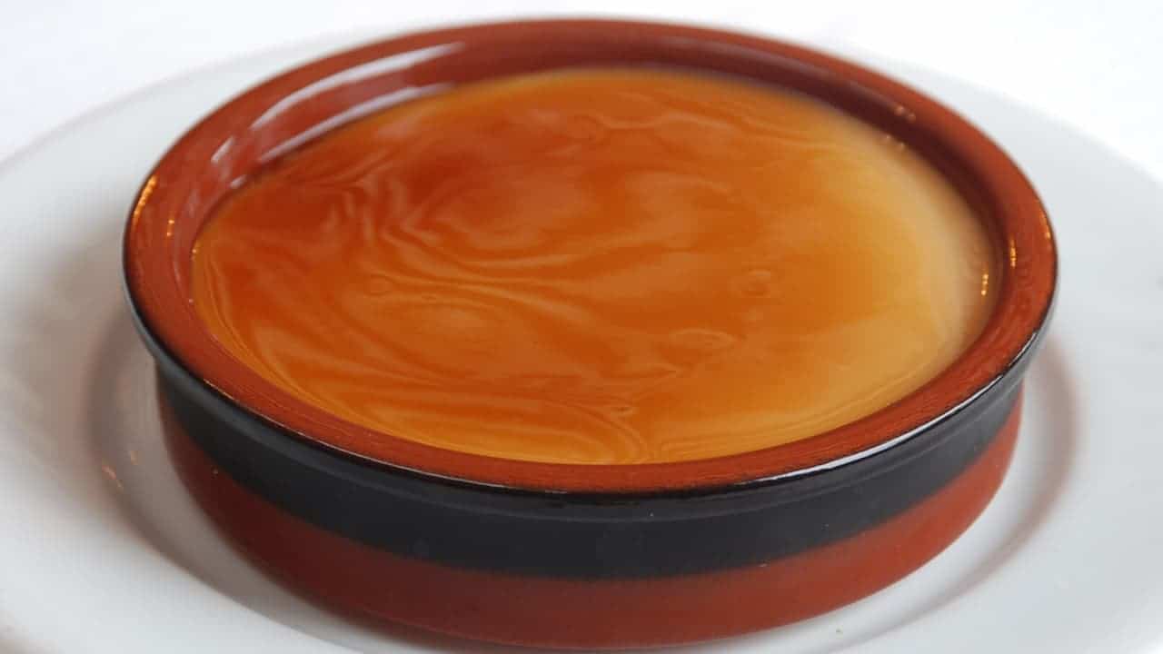 Round ceramic baking dish with glossy orange interior and dark brown exterior rim, sitting on white surface