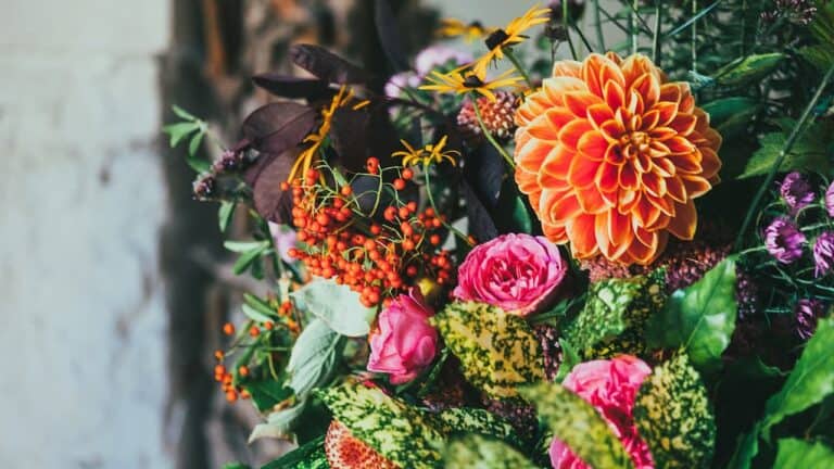 Vibrant autumn floral arrangement featuring orange dahlia, pink peonies, orange berries, dark foliage, and purple flowers in natural bouquet