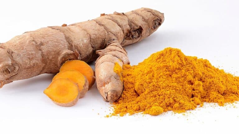 Fresh turmeric root with sliced pieces showing bright orange interior alongside pile of yellow turmeric powder