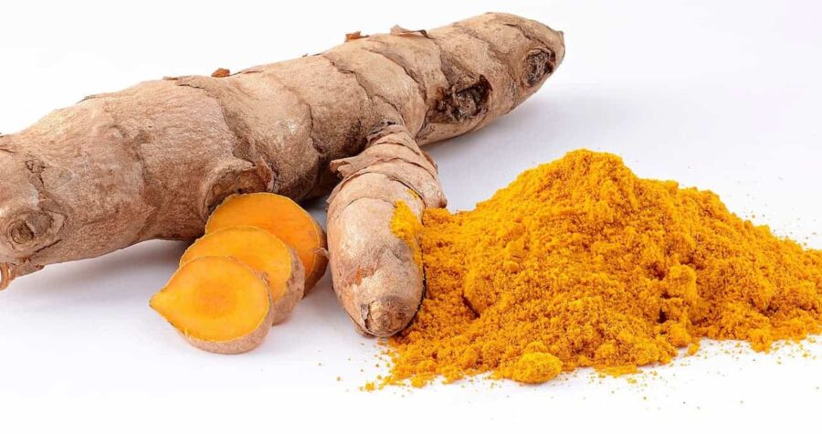 Fresh turmeric root with sliced pieces showing bright orange interior alongside pile of yellow turmeric powder