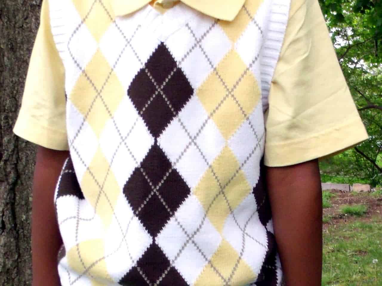 Close-up of a child wearing a yellow short-sleeve collared shirt layered with a sleeveless sweater vest featuring a white, yellow, and brown argyle pattern