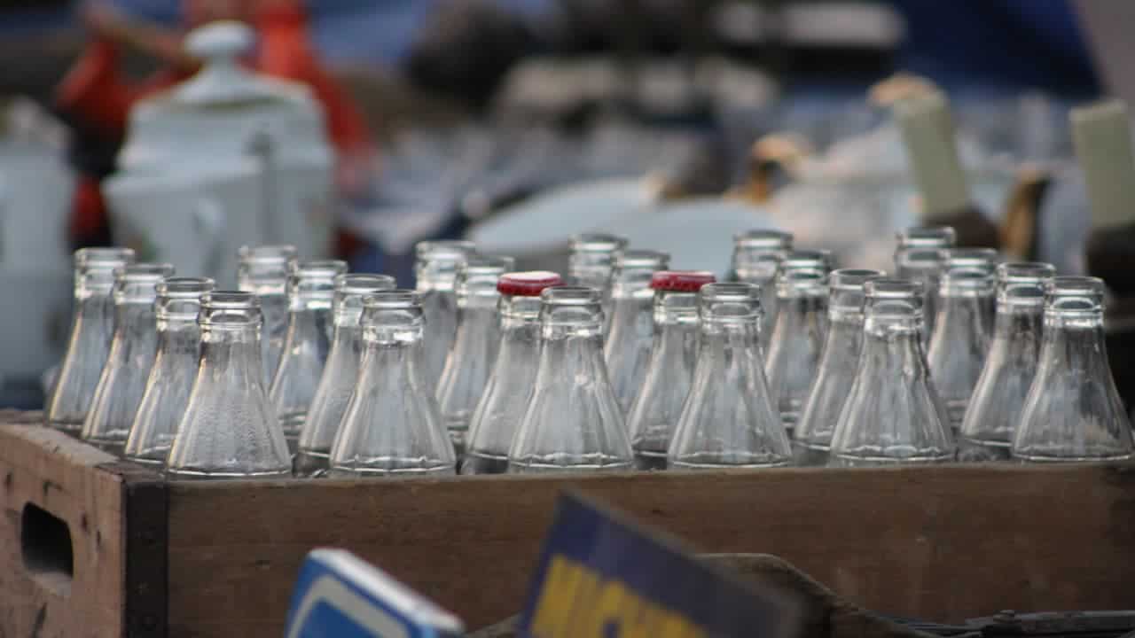 Wooden crate filled with empty glass bottles, some with red caps, set in a market or antique display