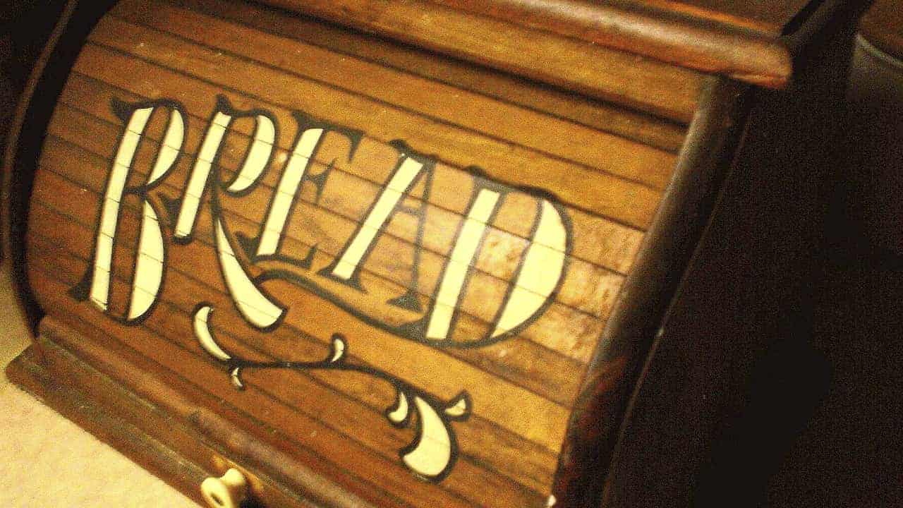 Wooden breadbox with a roll-top lid, featuring the word “BREAD” painted in large decorative white letters