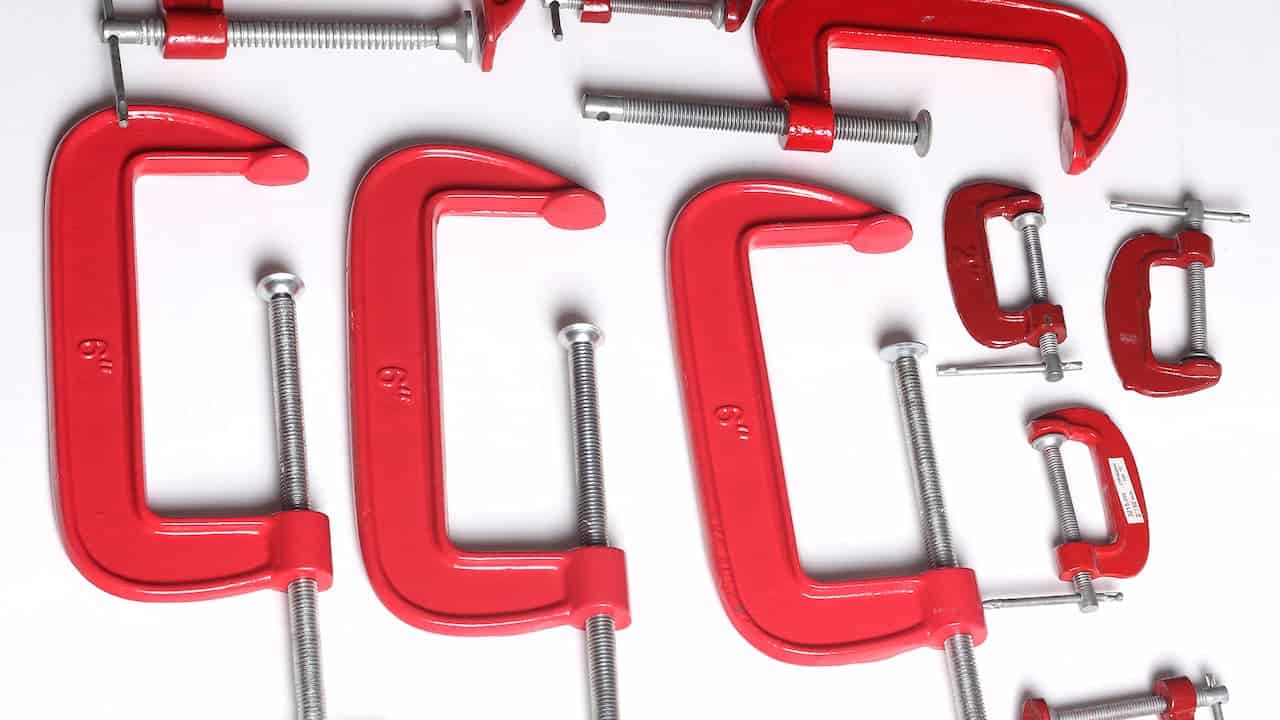 A collection of red C-clamps of various sizes arranged on a white background, showing their threaded screws and swivel pads used for clamping objects securely