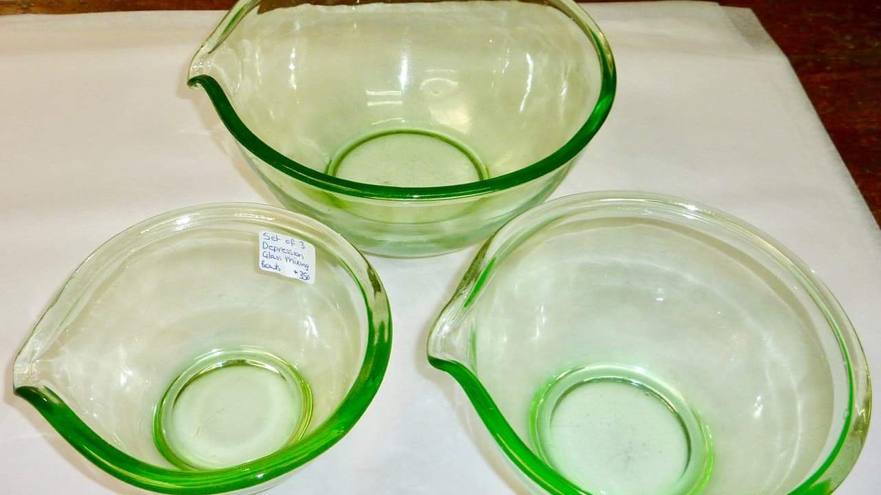 Three green-tinted glass mixing bowls with pour spouts, one labeled with price sticker, arranged on white surface