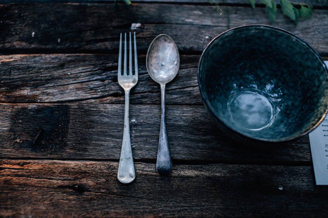 Vintage silver fork and spoon beside empty blue ceramic bowl on weathered wooden table surface