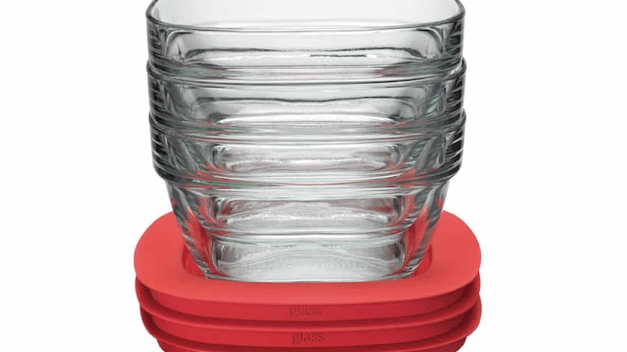 Stack of five clear glass rectangular food storage containers with matching red plastic lids on white background