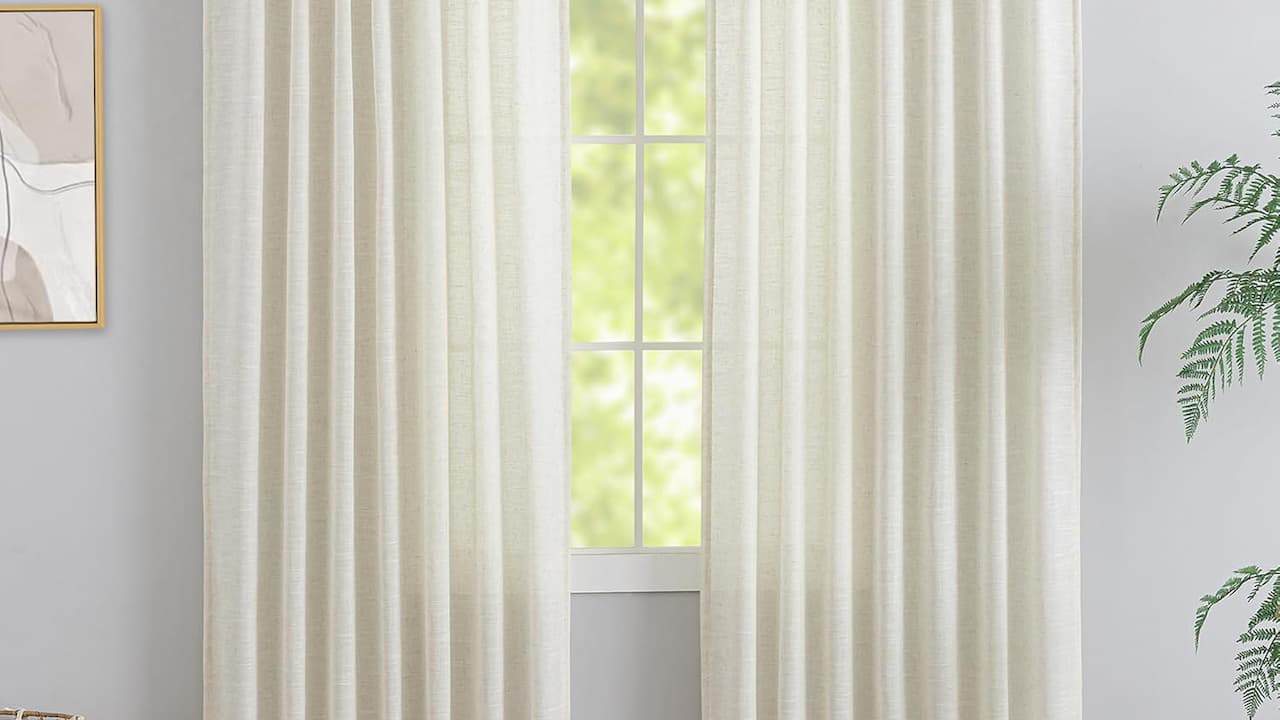  White or cream-colored curtains hanging in front of bright window with natural light filtering through