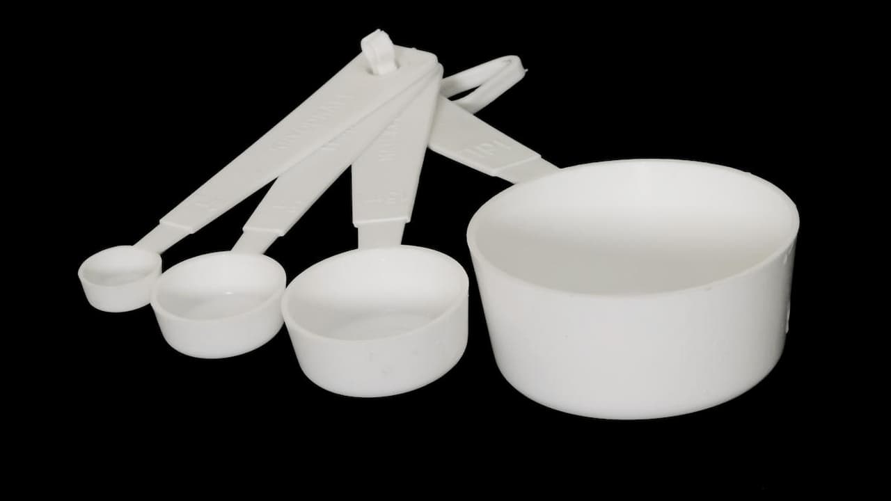 White plastic measuring cups and spoons set with long handles arranged on black background for cooking measurements