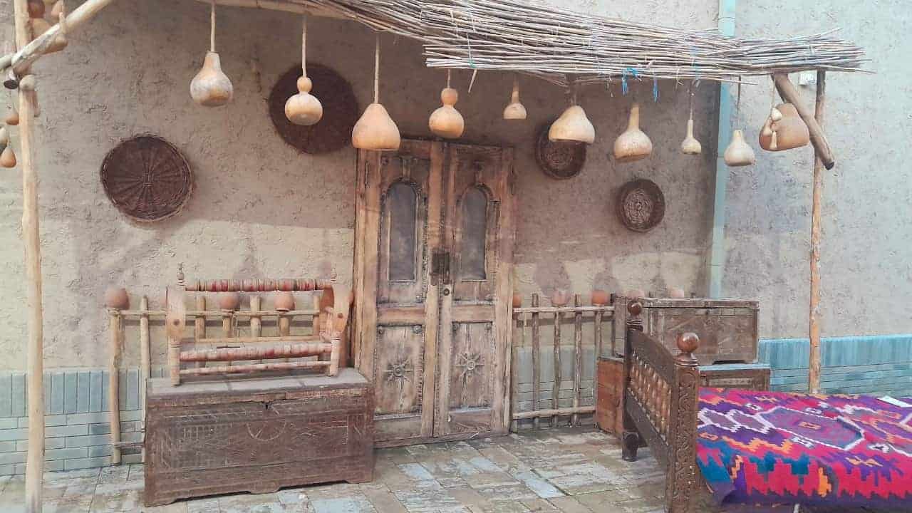 Rustic wooden door with hanging gourds under a reed canopy, surrounded by traditional furniture, woven baskets
