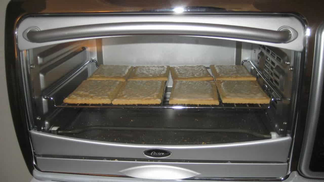 Oster toaster oven with glass door open, showing eight square crackers or pastries arranged on wire rack inside