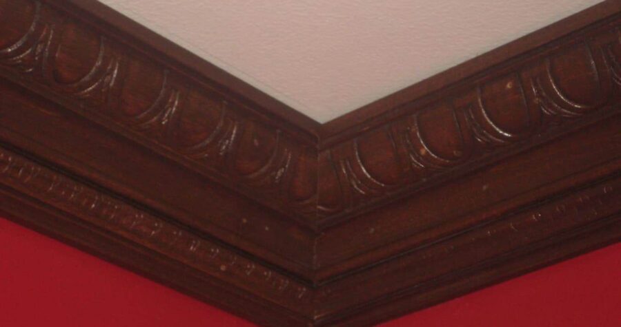 Decorative dark wood crown molding along the edge of a red wall and white ceiling corner