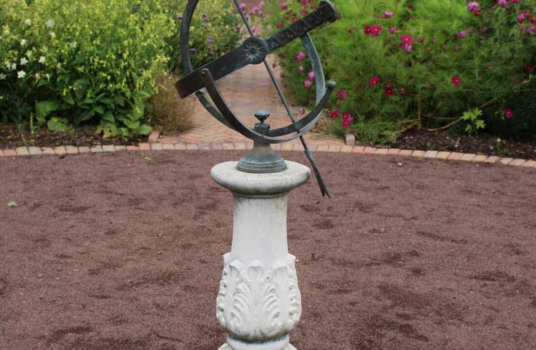 Garden sundial mounted on a pedestal, with a metal gnomon casting a shadow on engraved hour markers