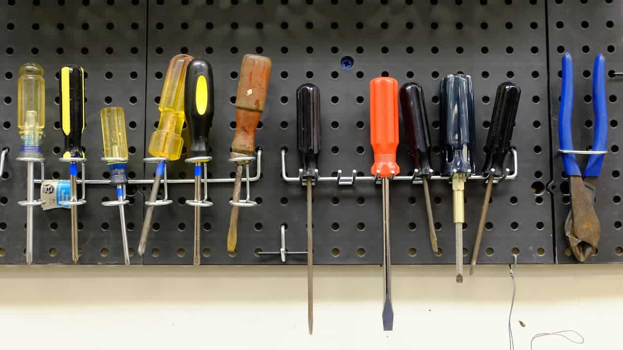 Tools neatly organized on a pegboard, hanging from hooks with outlines or labels, displayed in a workshop or garage