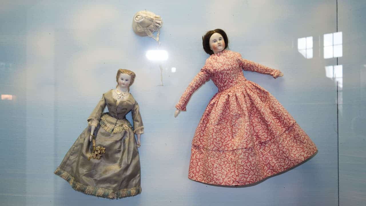 Two antique porcelain dolls in historical dresses displayed against a light blue background
