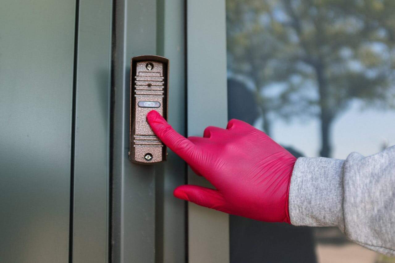 Person wearing bright pink rubber gloves pressing doorbell or intercom button on exterior wall