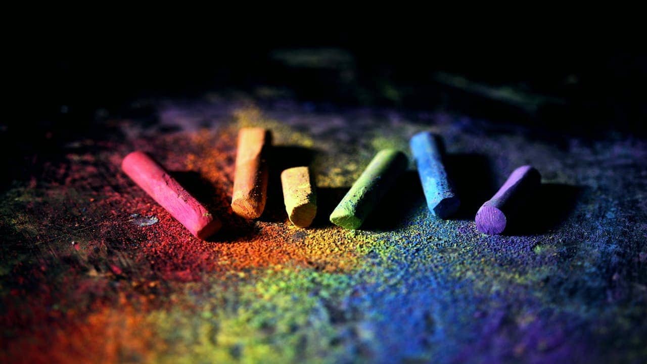 Colorful chalk pieces in red, yellow, green, and blue lying on rainbow chalk dust on dark surface