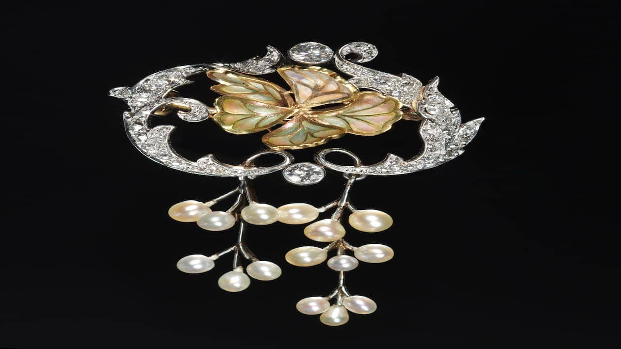 Ornate vintage brooch with diamond-encrusted scrollwork frame, central abalone shell flower motif, and cascading pearl drop dangles
