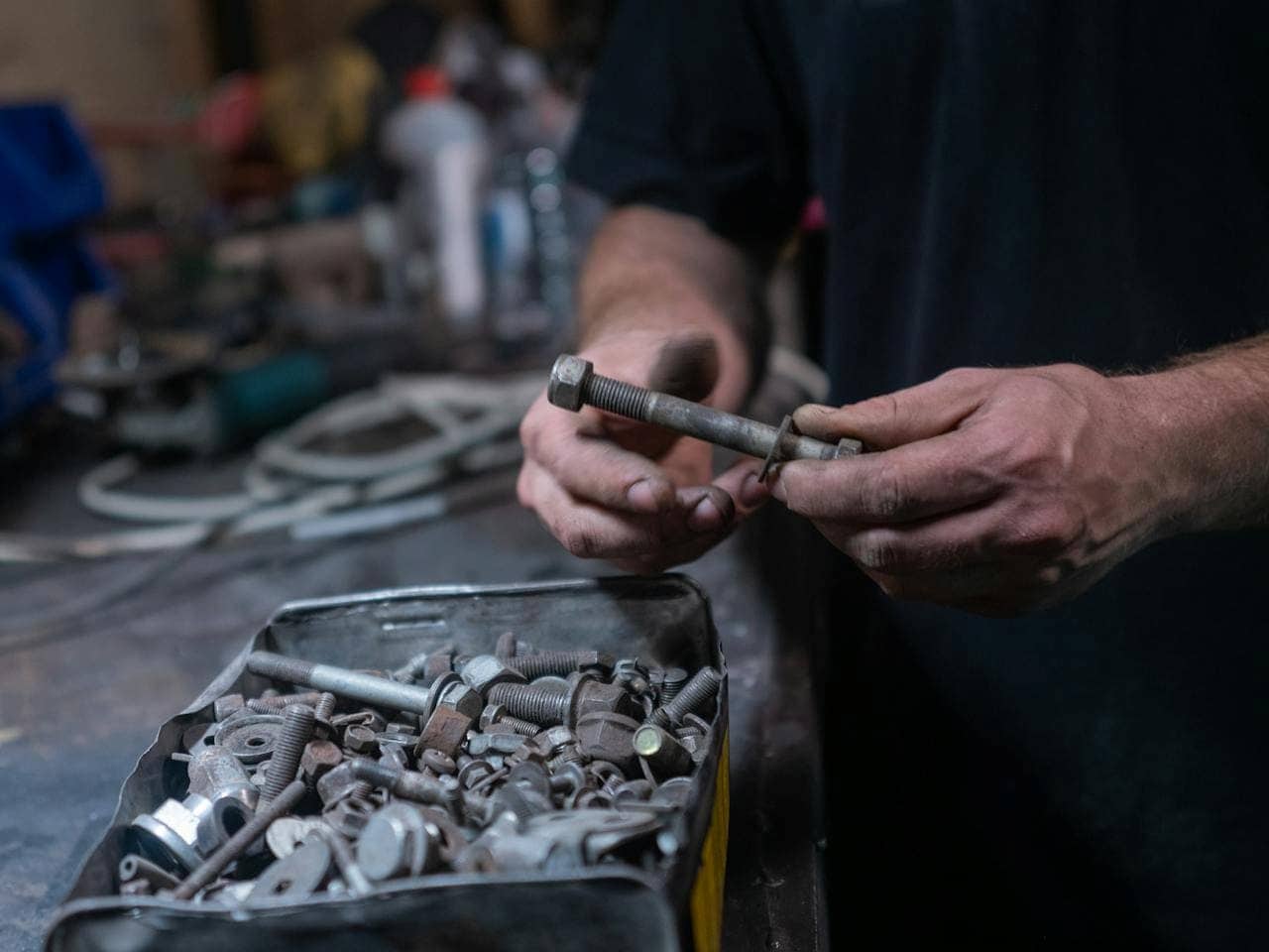  Person holding a large bolt while sorting through a metal tin drawer