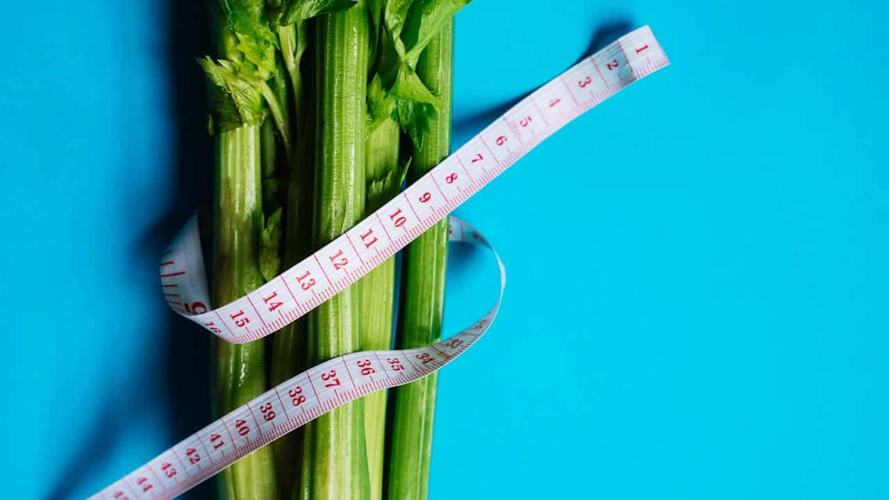 Fresh celery stalks wrapped with a white measuring tape against a bright blue background