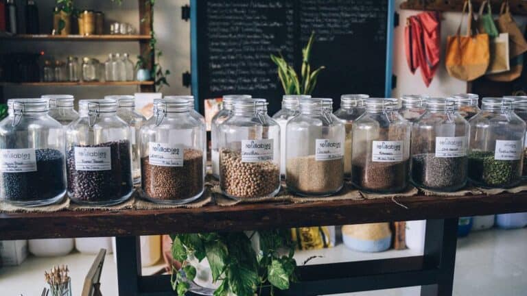 Glass jars with hinged lids containing various seeds, beans, and grains displayed on wooden table in sustainable refill store