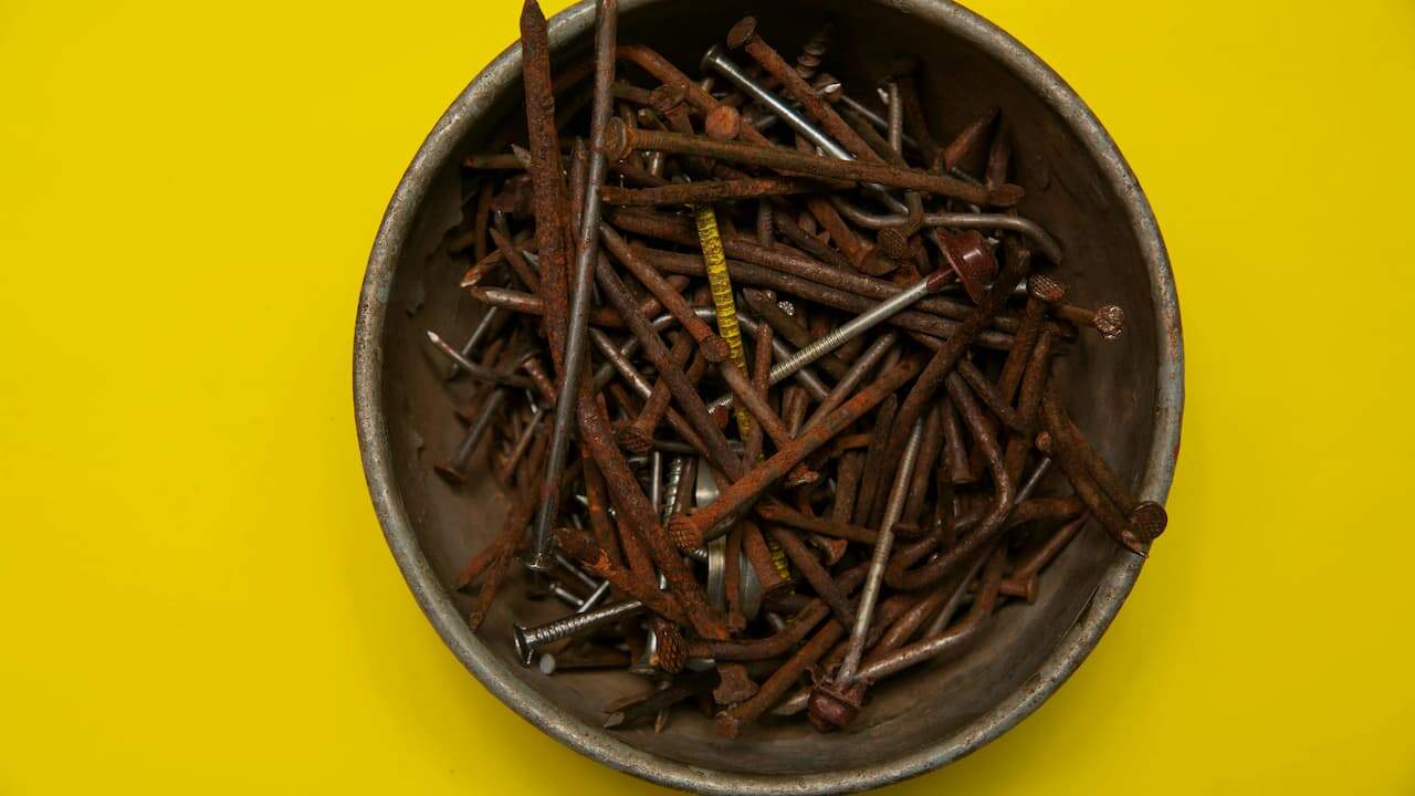 Rusty nails collected in a bowl, showing corroded surfaces and reddish-brown oxidation