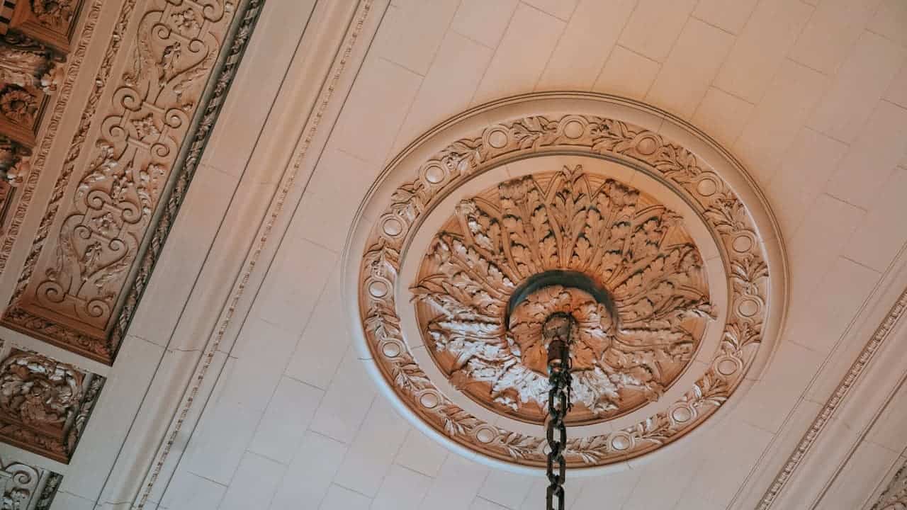 Ornate ceiling medallion with intricate carved floral and leaf patterns surrounding central light fixture chain in classical interior
