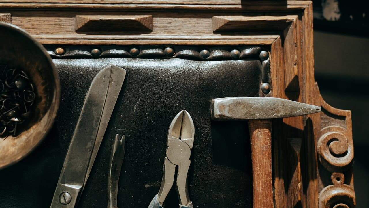 Vintage antique tools including straight razor, pliers, and knife displayed on dark leather surface with studded trim and wooden storage