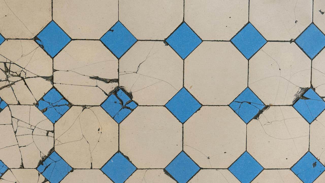 Patterned floor tiles with a cream base and blue diamond-shaped accents, several tiles showing visible cracks and signs of wear