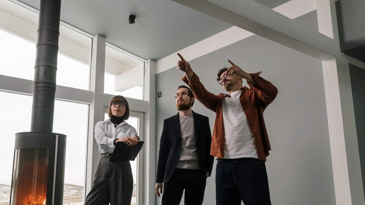 Three design professionals discussing project in modern office with large windows, fireplace, and one person gesturing upward