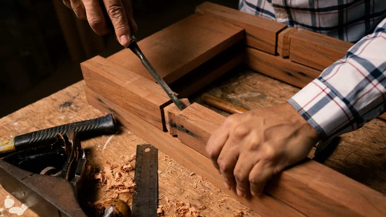 A woodworker using a chisel to shape a wooden joint on a workbench