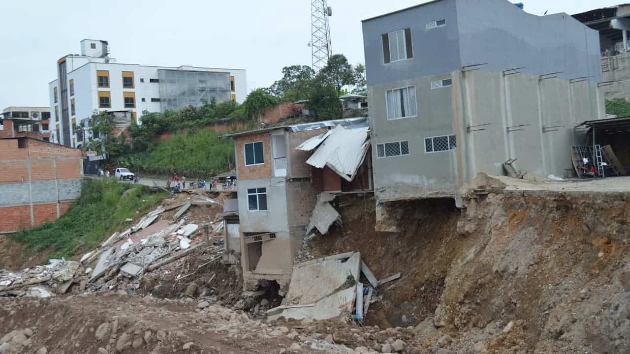 Severe soil erosion and landslide damage around residential buildings with collapsed foundations and exposed structural elements