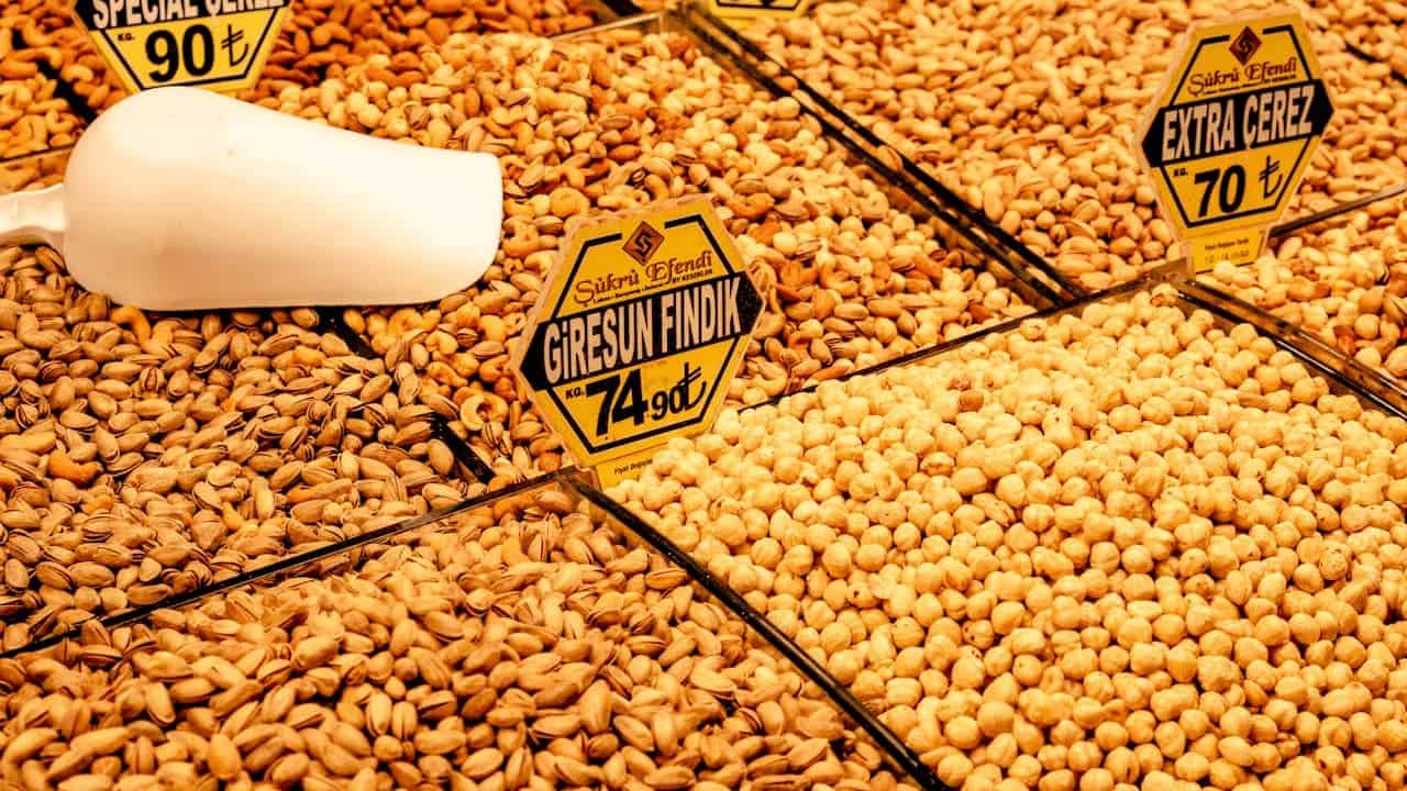 Bulk display of organic nuts and legumes with Turkish price signs including pistachios, hazelnuts, and chickpeas in market bins