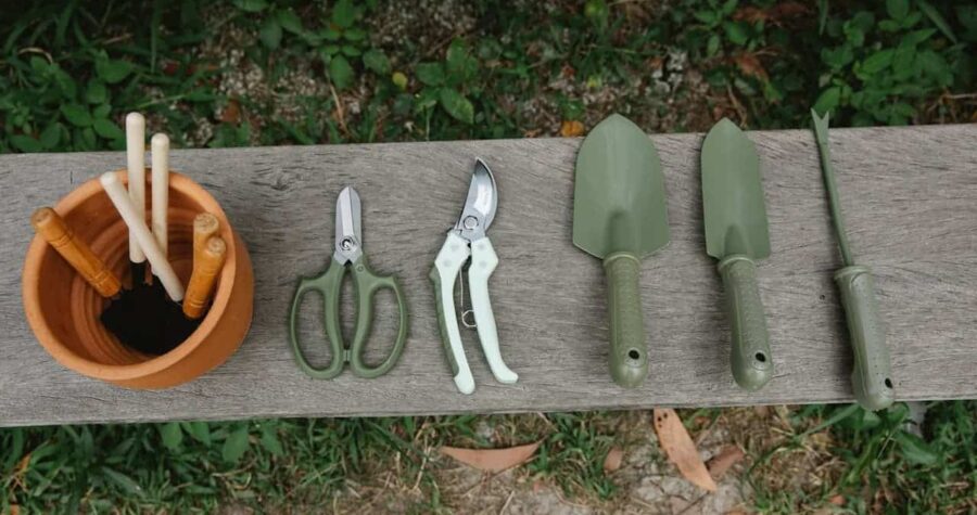Garden tools laid out on wooden bench including pruning shears, hand trowels, and cleaning supplies for maintenance