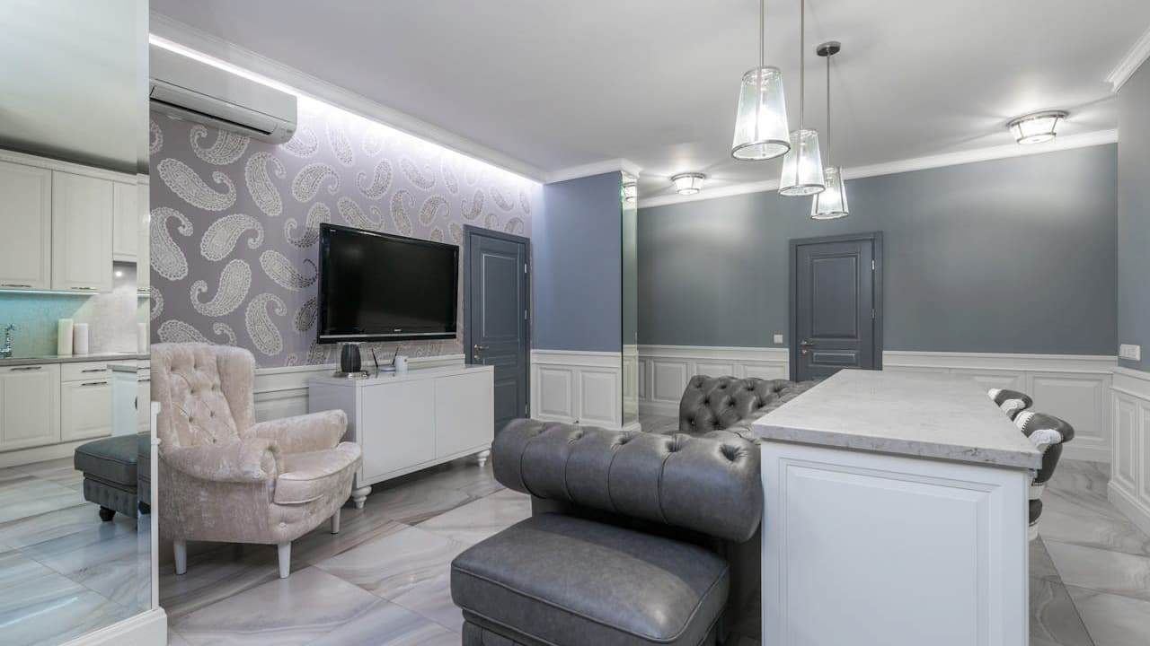 Modern living room with gray upholstered sofa, beige tufted armchair, white kitchen island, and contemporary interior design