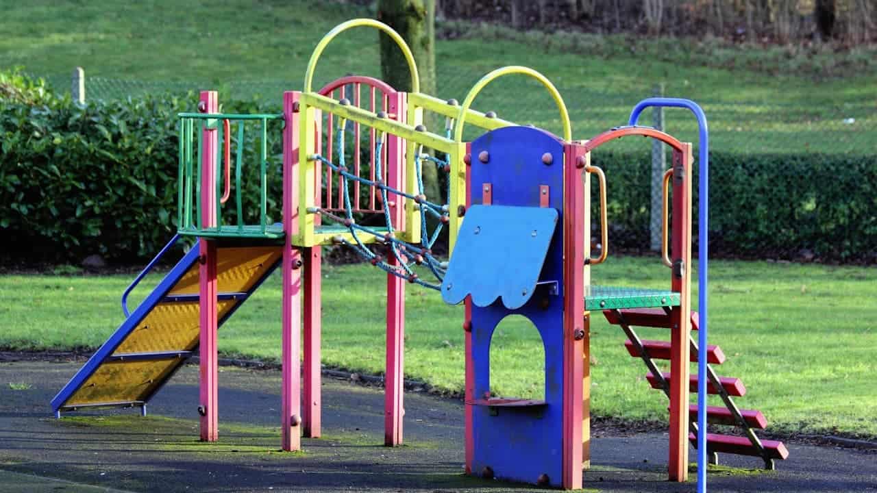 Colorful children's playground equipment with slides, climbing structures, and safety railings on rubber surfacing in park setting