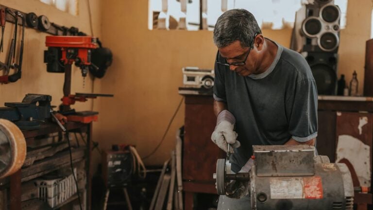 Man working with a bench grinder in a workshop, wearing gloves and safety glasses