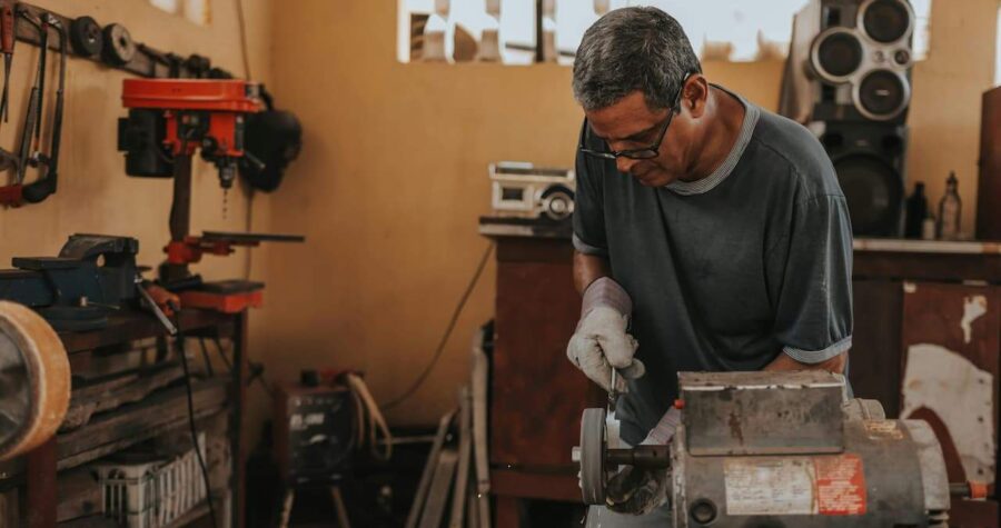 Man working with a bench grinder in a workshop, wearing gloves and safety glasses