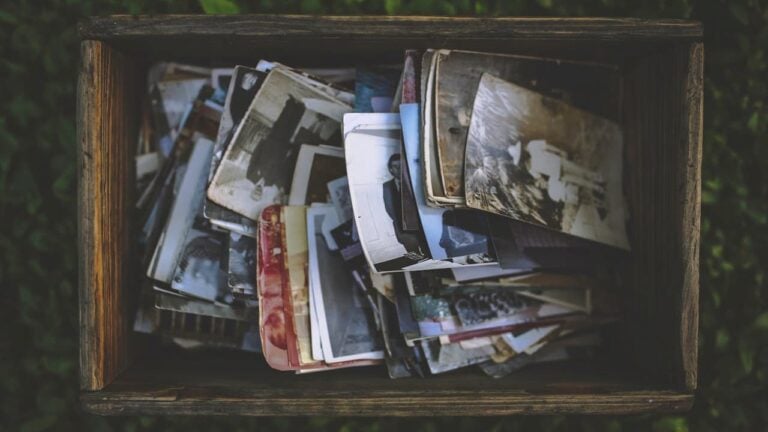 Wooden box filled with scattered vintage photographs, both black-and-white and color prints, creating a nostalgic collection of old memories