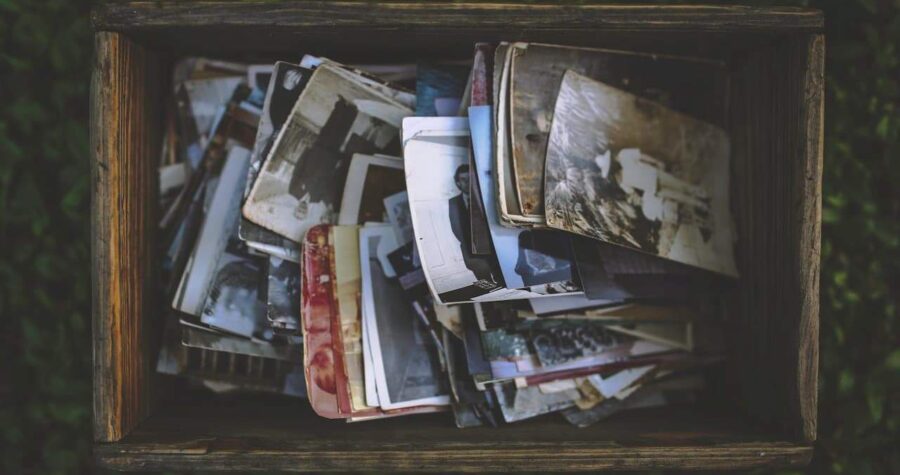 Wooden box filled with scattered vintage photographs, both black-and-white and color prints, creating a nostalgic collection of old memories