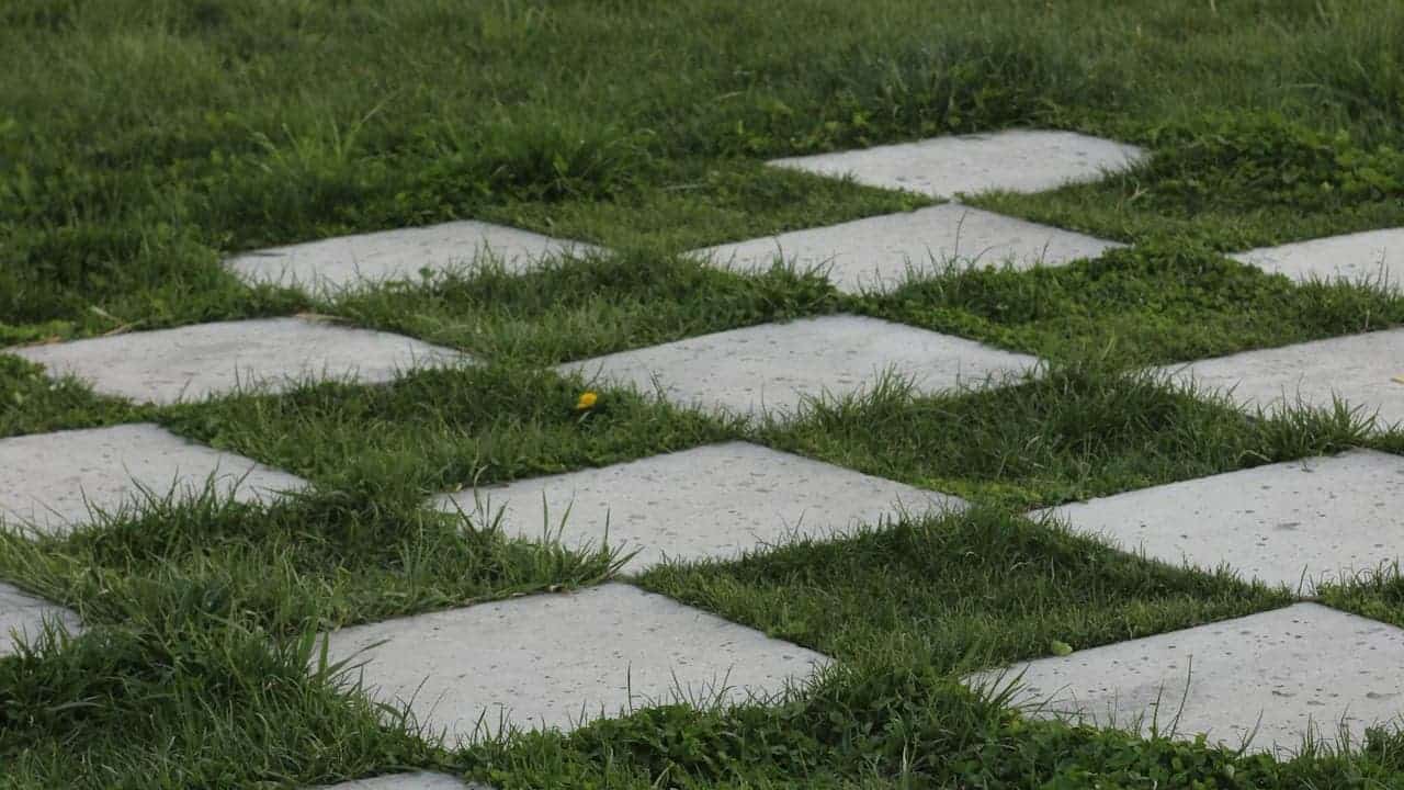 Checkerboard pattern of alternating concrete square pavers and green grass sections creating geometric landscape design