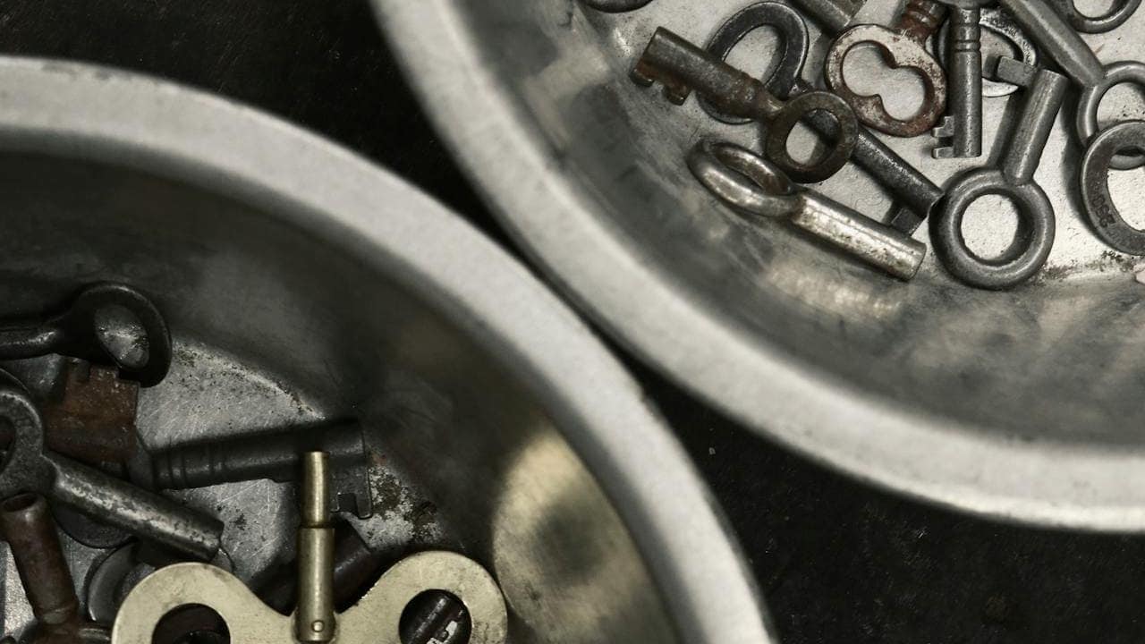 Close-up of two metal bowls containing a collection of old, assorted keys and a clock winding key, with visible wear and tarnish