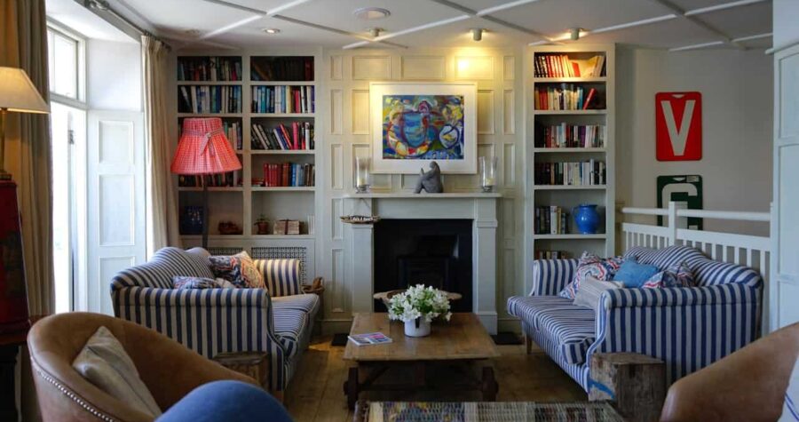 Cozy living room with blue striped sofas, built-in bookshelves, fireplace, wooden coffee table, and brown leather chairs in cramped arrangement