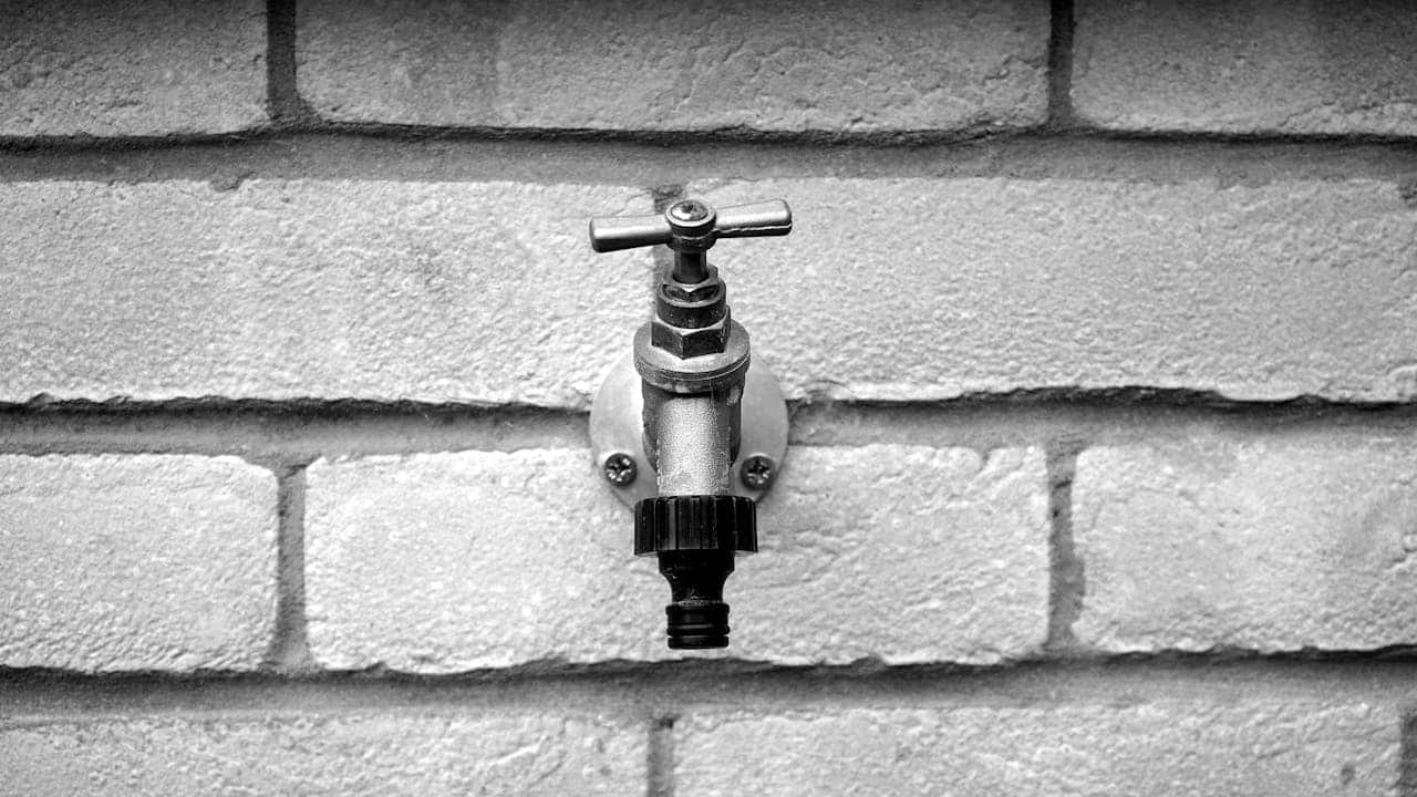 Metal outdoor faucet mounted on a brick wall in black and white
