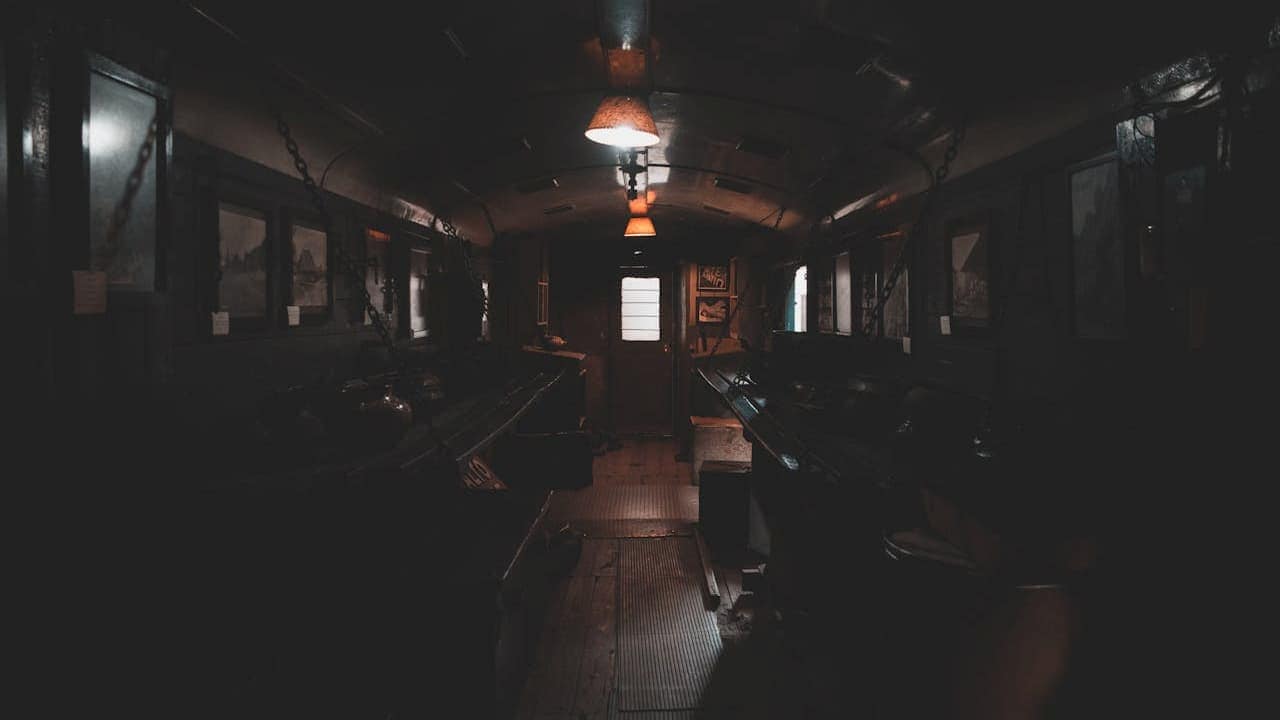 Dark interior of room with wooden benches, hanging lamps, and windows letting in natural light through dimly lit space