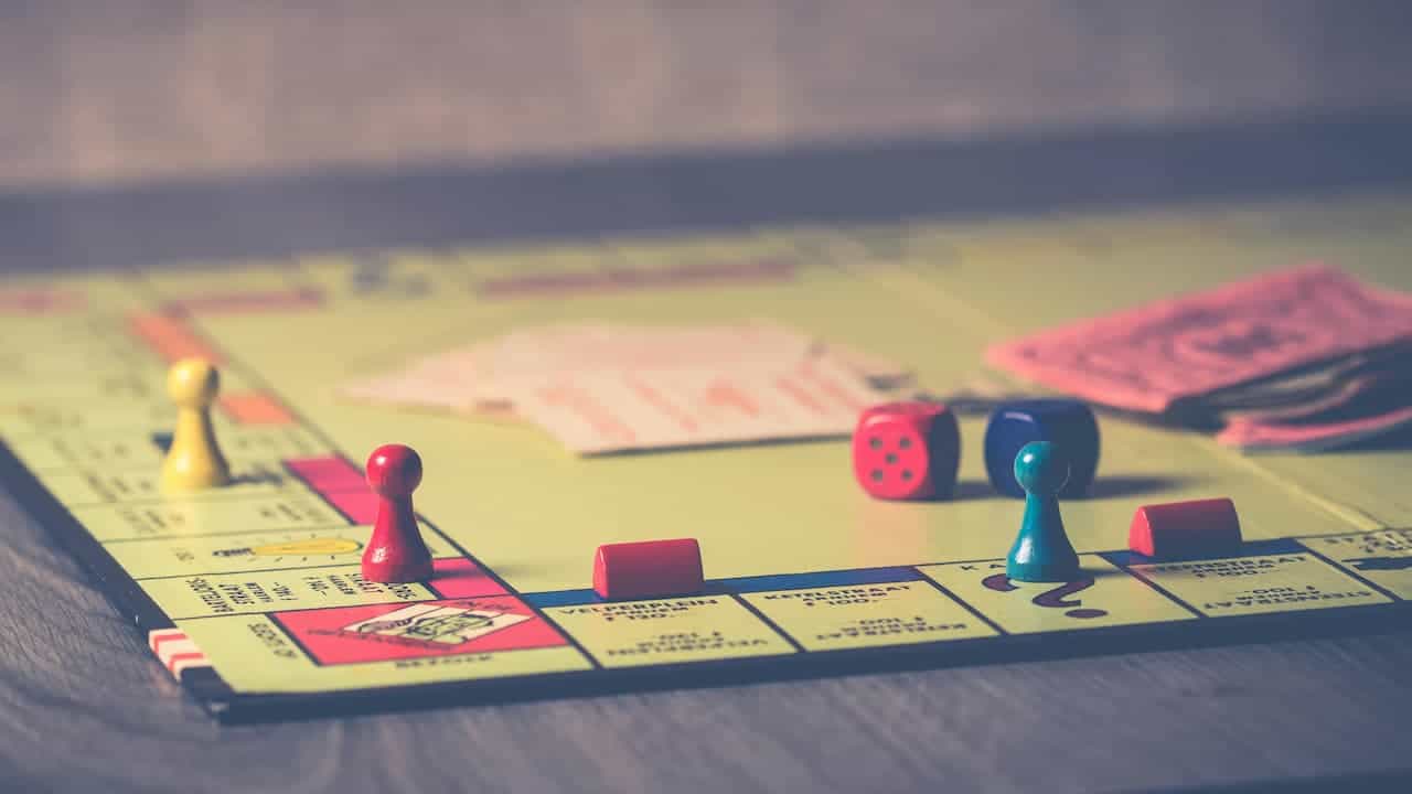  A close-up of a Monopoly board game in play, showing colorful game pieces, dice, pink Monopoly money
